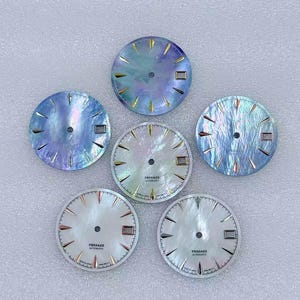 Puede incluir: Seis esferas de reloj con superficies iridiscentes y nacaradas. Las esferas presentan marcadores de hora y agujas doradas, con la palabra "PRESAGE AUTOMATIC" impresa en algunas. Los colores var&iacute;an del azul al blanco.