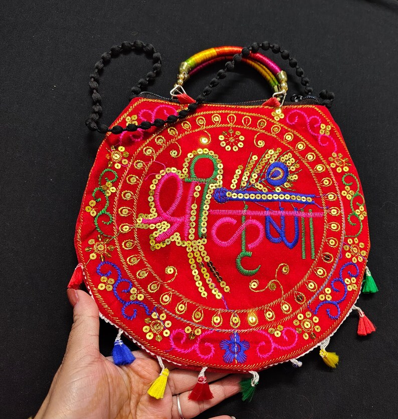 Puede incluir: Un bolso rojo bordado con un dise&ntilde;o circular con lentejuelas doradas e hilo de colores. El bolso tiene una correa de cuentas y un asa de color arco&iacute;ris. Borlas de varios colores cuelgan de la parte inferior.