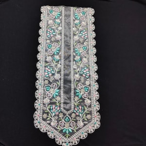 Op de afbeelding: Een transparante, grijze stoffen rand met ingewikkelde bloemenborduurwerk. Het ontwerp toont turquoise, roze en witte bloemen met groene bladeren, omzoomd door een geschulpte rand. Geschikt voor het verfraaien van kleding of knutselprojecten.