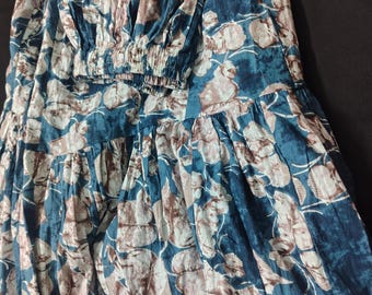 Könnte beinhalten: Ein langer Rock mit einem tiefblauen und weißen Blumenmuster und einem gerafften, gestuften Design. Der Stoff hat eine knittrige Textur und der Bund ist elastisch mit einem gerafften Abschluss, was eine voluminöse, fließende Silhouette erzeugt.