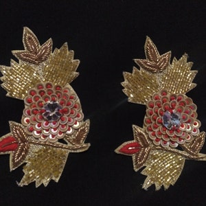 Può includere: Due applicazioni floreali ricamate in oro e rosso con paillettes e un centro di cristallo.