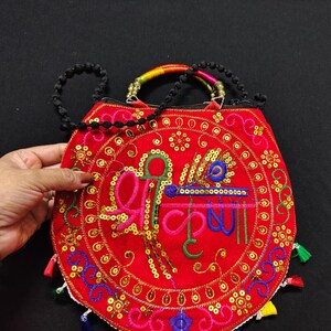 Puede incluir: Bolso bordado rojo con un dise&ntilde;o circular con lentejuelas doradas e hilo colorido. El bolso tiene una correa de cuentas negras y un asa arco&iacute;ris. El dise&ntilde;o incluye texto multicolor.