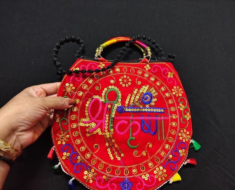 Puede incluir: Bolso bordado rojo con un dise&ntilde;o circular con lentejuelas doradas e hilo colorido. El bolso tiene una correa de cuentas negras y un asa arco&iacute;ris. El dise&ntilde;o incluye texto multicolor.