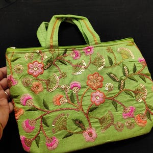 May include: A small green purse with floral embroidery and sequins. The purse has a top handle and a zipper closure.