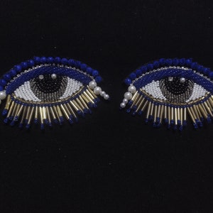 May include: Two blue evil eye charms with white and black bead details. The charms have gold accents and white pearl accents.