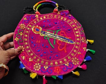 Puede incluir: Un bolso redondo de color magenta con intrincados bordados y adornos. El bolso presenta un asa arcoíris, lentejuelas doradas y borlas coloridas. El diseño incluye un motivo central bordado con texto.