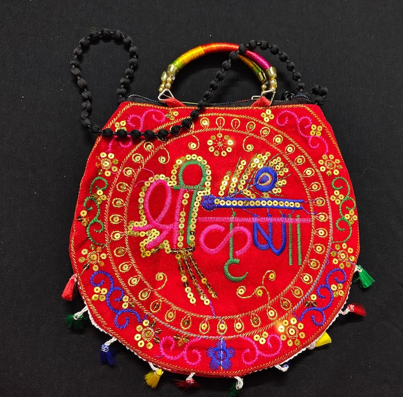 Puede incluir: Bolso de mano rojo bordado con un dise&ntilde;o circular con texto colorido y adornos. El bolso tiene una correa de cuentas negras y un asa con detalles de arco&iacute;ris. Peque&ntilde;as borlas de varios colores adornan el borde inferior.