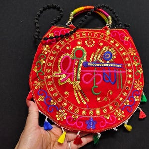 Puede incluir: Bolso de mano rojo bordado con lentejuelas doradas y borlas coloridas. El bolso presenta un dise&ntilde;o central con texto en verde y azul, un asa de cuentas negras y un asa superior de arco&iacute;ris.