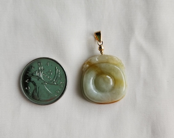 Puede incluir: Un colgante de jade con una argolla de oro. El colgante está tallado en forma de círculo con un círculo más pequeño en el centro. El jade es de color verde claro con vetas marrones.