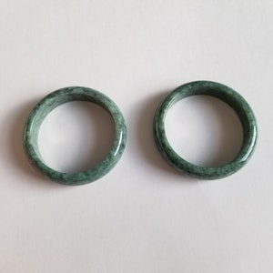 May include: Two green jade bangle bracelets. The bracelets are smooth and polished, with a mottled green colour.