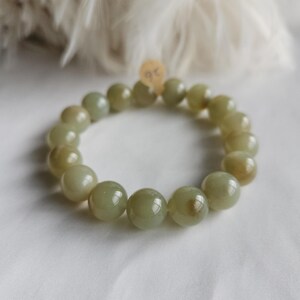 May include: A bracelet featuring smooth, light green beads. The beads are strung together, creating a circular design. The bracelet is presented on a white surface. Each bead is approximately 1.5 cm in diameter.