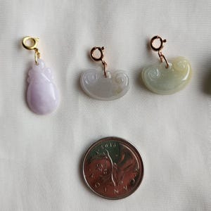 May include: Three jade pendants with gold-tone clasps. The pendants are carved with different designs. One is a pale purple, one is a pale green, and one is a pale green with a yellow hue.