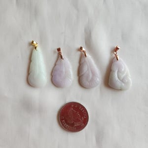 May include: Four jade pendants with gold accents. The pendants are carved in the shape of leaves and have a light purple hue. The pendants are arranged in a row on a white surface.
