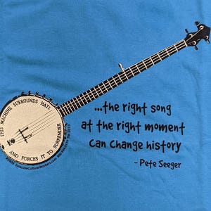 May include: A blue t-shirt with a black and white illustration of a banjo and a quote by Pete Seeger: "...the right song at the right moment Can Change history - Pete Seeger"