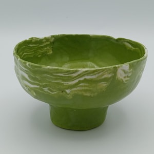May include: A ceramic bowl with a vibrant green glaze and white marbling. The bowl has a pedestal base and a slightly uneven rim. This decorative bowl is suitable for serving or display.