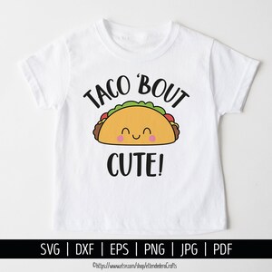 May include: A white short-sleeved t-shirt featuring a graphic of a smiling taco with pink cheeks, green lettuce, and brown meat. The text above the taco reads TACO 'BOUT and the text below reads CUTE! in a bold, black, sans-serif font.