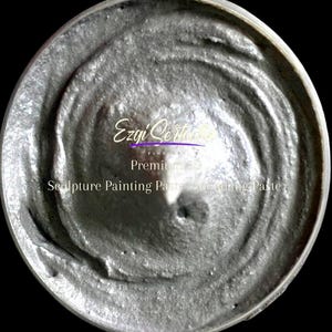 Könnte beinhalten: Ein runder Behälter gefüllt mit einer dicken, metallisch silbernen Skulpturen-Malpaste. Die Oberfläche der Paste hat ein gewirbeltes, strukturiertes Aussehen. Der Text "Ezgi Sertoğlu Premium 3D Sculpture Painting Paste - Modeling Paste" ist in Weiß aufgedruckt.
