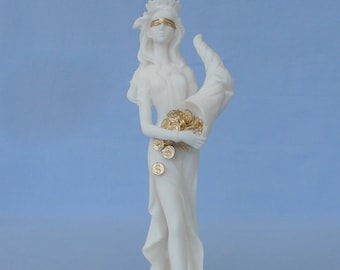 May include: A white statue of a woman with a blindfold and a cornucopia overflowing with gold coins. The statue has gold accents on the blindfold, coins, and feet. The statue is on a white base with gold coins scattered around.