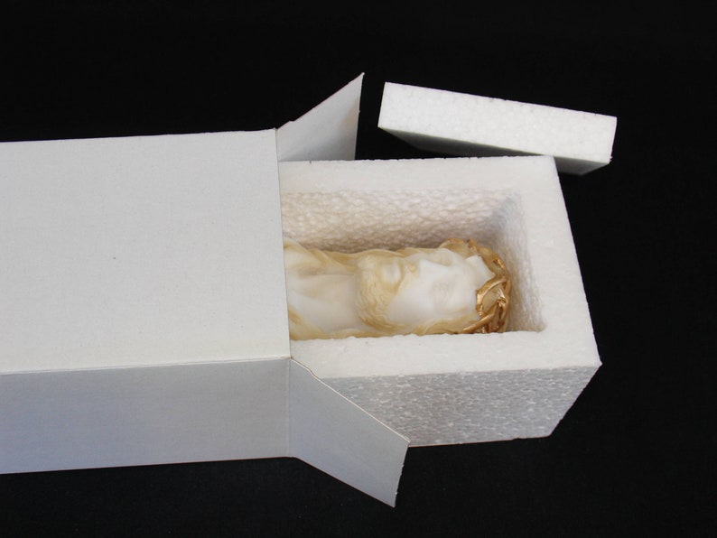 May include: A white plaster sculpture of a person's head with a gold crown of thorns, inside a white styrofoam box with a white cardboard lid.