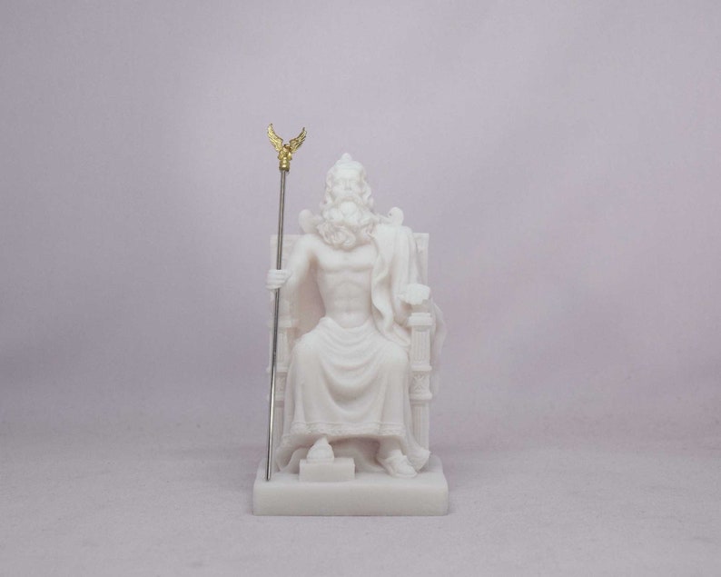 May include: A white statue of Zeus, seated on a throne, holding a staff with a gold-colored winged emblem. The sculpture features detailed facial hair and drapery, and is set against a plain background.