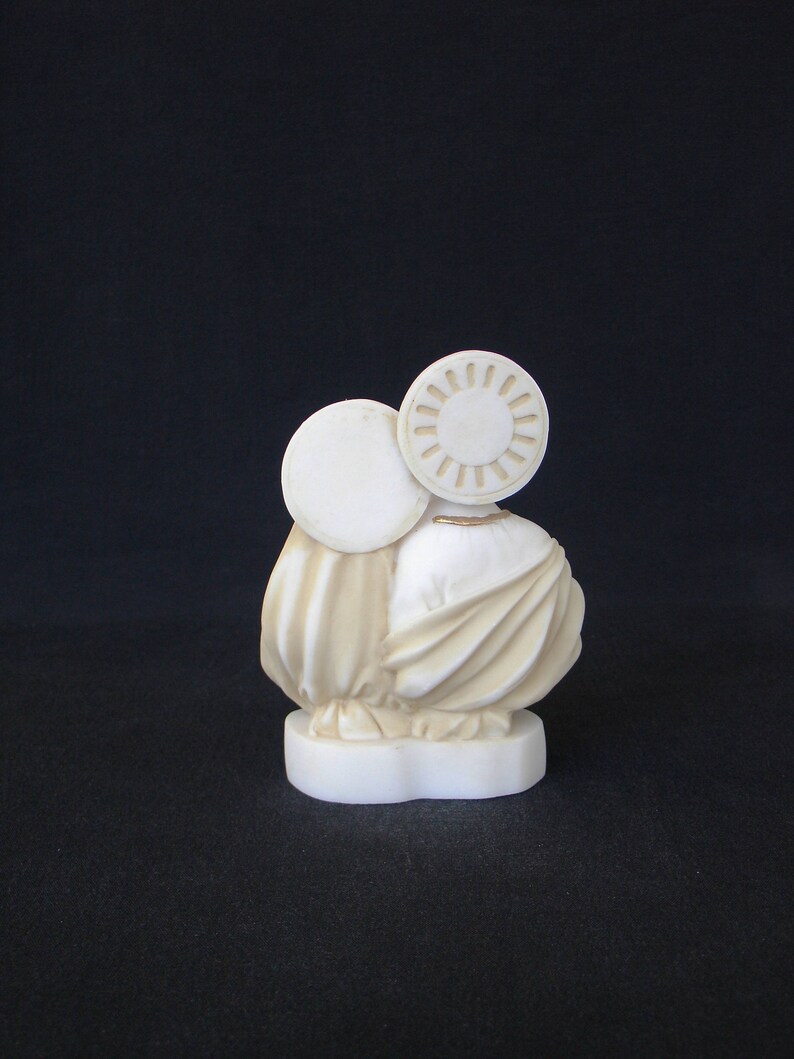 Peut inclure: Sculpture en c&eacute;ramique blanche de deux personnages, l'un avec une aur&eacute;ole ronde, debout sur une base blanche. Les personnages sont v&ecirc;tus de robes flottantes.