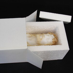 May include: A white plaster sculpture of a person's head with a gold crown of thorns. The sculpture is inside a white styrofoam box with a white cardboard lid.