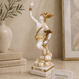 Op de afbeelding: Een wit en goudkleurig standbeeld van de Griekse god Hermes, afgebeeld met een gevleugelde helm en sandalen, terwijl hij een caduceus vasthoudt. Het figuur staat op een rechthoekige voet met de Griekse tekst EPMHE en gouden accenten.