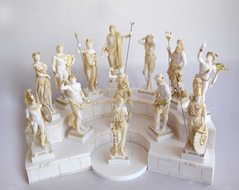 May include: A set of twelve white and gold Greek god and goddess figurines on a white base. The figurines are arranged in a circle and each has a different pose and expression. The base is decorated with gold trim and the names of the gods and goddesses are written on the base.