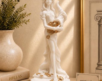 May include: A white statue of a blindfolded figure wearing a crown and holding a cornucopia overflowing with gold coins. The figure stands on a base scattered with gold coins. A small sign nearby displays the text estatueshop greek statues.