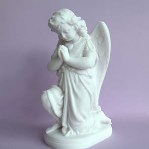 May include: White marble statue of a kneeling angel with wings, praying with hands clasped together. The angel is wearing a flowing robe and has a pearl necklace.