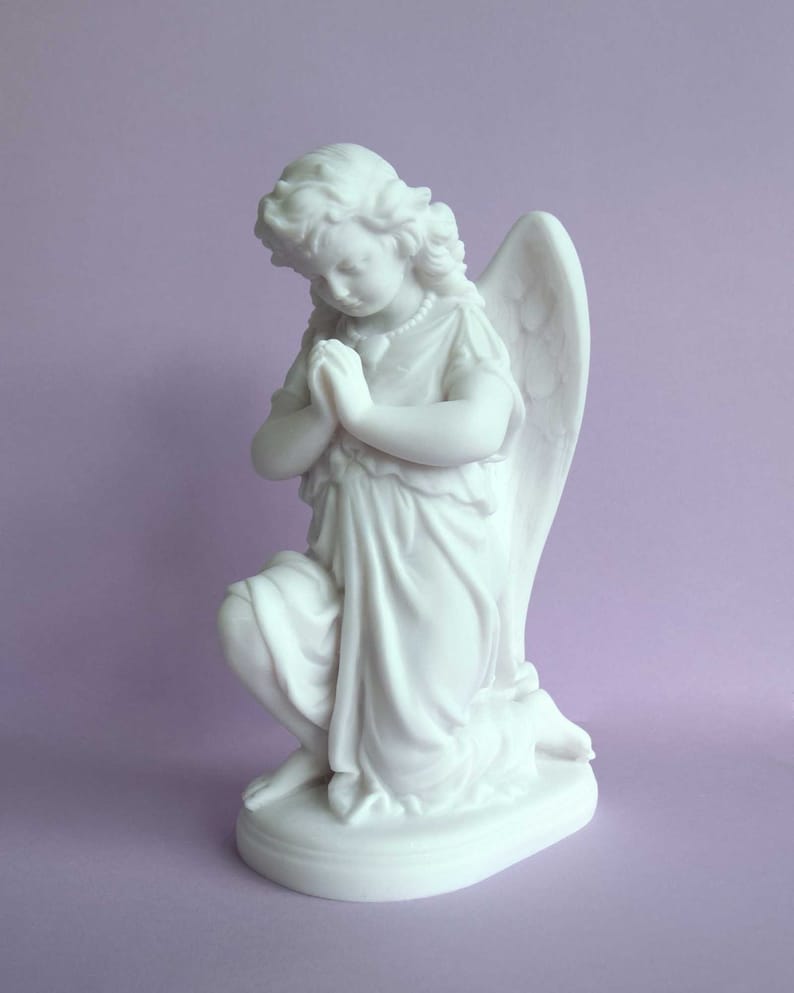 May include: White marble statue of a kneeling angel with wings, praying with hands clasped together. The angel is wearing a flowing robe and has a pearl necklace.