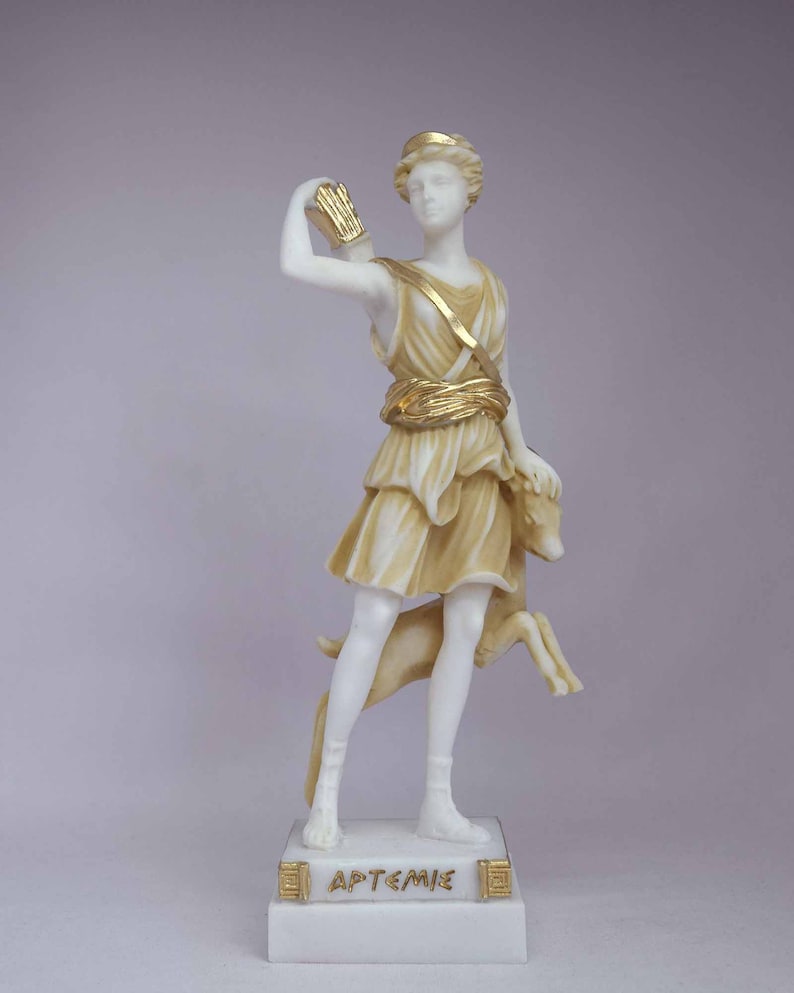 May include: A white marble statue of Artemis, the Greek goddess of the hunt, with gold accents. She is holding a bow and arrow in her right hand and a deer in her left hand. The statue is standing on a white marble base with the inscription "&Alpha;&Rho;&Tau;&Epsilon;&Mu;&Iota;&Sigma;" in gold letters.