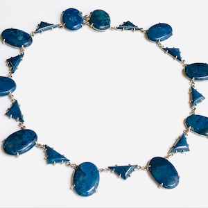 May include: A silver necklace with oval-shaped blue stones and triangular silver accents.