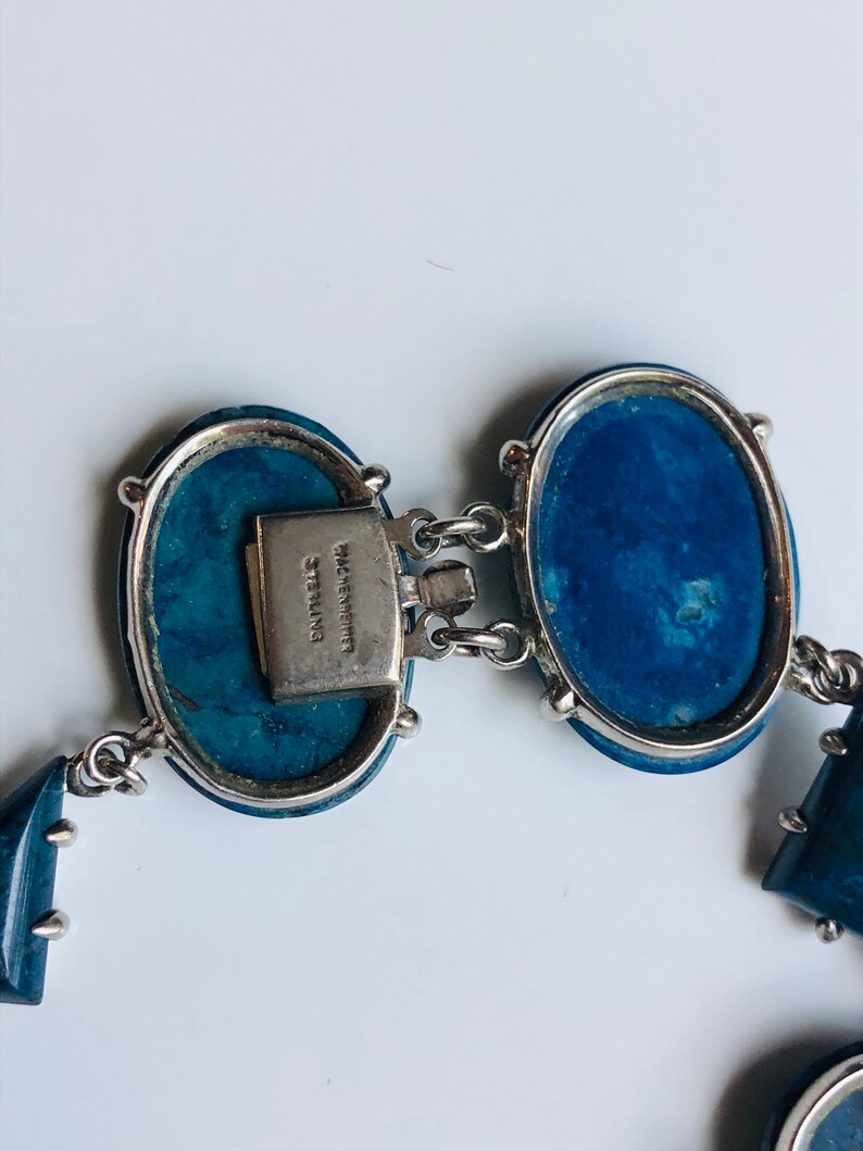 May include: A blue and silver bracelet with oval-shaped stones and a clasp that reads "Wm. Spraragen Sterling".