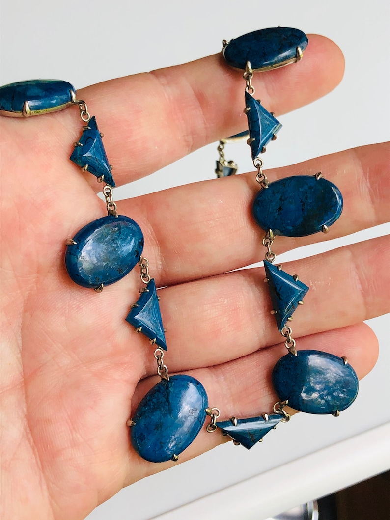May include: A silver chain necklace with oval and triangular blue gemstone accents.