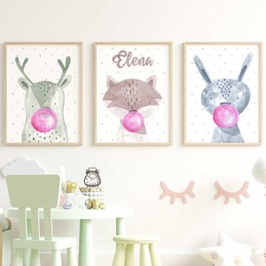 Puede incluir: Tres impresiones de animales en acuarela con chicle rosa. Las impresiones representan un ciervo, un zorro y un conejo. Las impresiones están enmarcadas en madera clara y tienen un fondo blanco con pequeños puntos blancos.