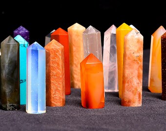 May include: A collection of colorful gemstone obelisks. The crystals vary in color, including orange, yellow, clear, blue, and brown. Each obelisk has a pointed top and a rectangular base. The background is dark.