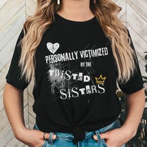 May include: Black t-shirt with a white broken heart, the text "PERSONALLY VICTIMIZED BY THE TWISTED SISTERS" and a gold crown.