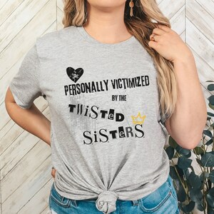 May include: Gray t-shirt with a black broken heart and the text "PERSONALLY VICTIMIZED BY THE TWISTED SISTERS" in black with a gold crown.