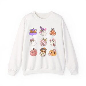 May include: White sweatshirt featuring a repeating pattern of cartoon ghosts and pumpkins. The ghosts are wearing hats and bows, and the pumpkins have floral accents. The design includes shades of purple, orange, pink, and green.