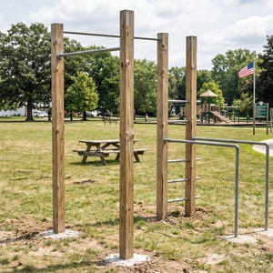 May include: Outdoor wooden workout structure with pull-up bars, parallel bars, and a ladder. The structure is set in a grassy park with picnic tables, a playground, and an American flag waving in the background.