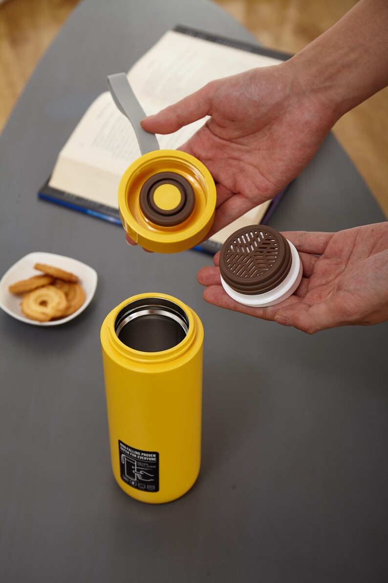 May include: A yellow stainless steel water bottle with a brown and white lid. The lid has a removable filter. The bottle has a black label that says "Double Power Keep It Fresh For Everyone".