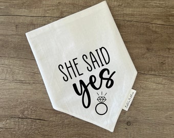 May include: White cotton bandana with black text that reads "She Said Yes" and a diamond ring illustration. The bandana has a small white tag with the text "Brittni Bullen" on it.