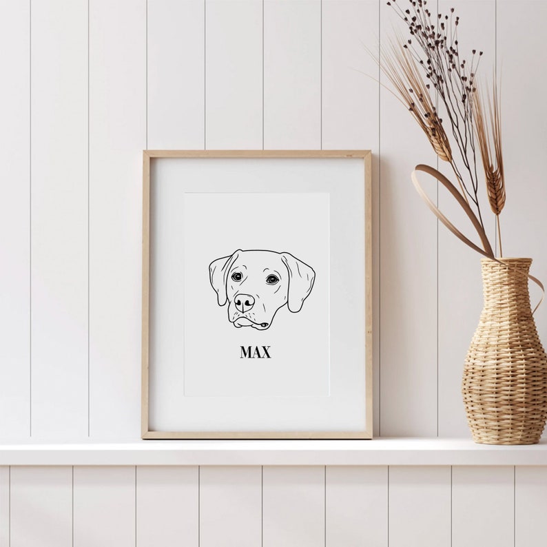 May include: A black and white line drawing of a dog's head with the name Max printed below it. The drawing is framed in a light wood frame and is displayed on a white shelf.