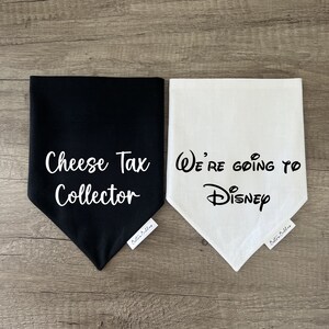 K&ouml;nnte beinhalten: Zwei dreieckige Haustierhalst&uuml;cher, eines in Schwarz mit wei&szlig;em Text Cheese Tax Collector und eines in Wei&szlig; mit schwarzem Text We're going to Disney. Jedes Halstuch hat ein kleines wei&szlig;es Stoffetikett mit dem Markennamen Bestie Buddies.