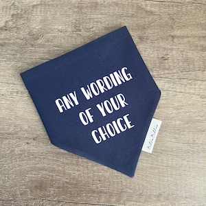K&ouml;nnte beinhalten: Ein dreieckiges Bandana aus marineblauem Stoff mit dem wei&szlig;en Text ANY WORDING OF YOUR CHOICE in einer serifenlosen Schriftart. Ein kleines wei&szlig;es Stoffetikett mit dem schwarzen Text Bexton Buddies ist an der rechten Seite des Bandanas befestigt.