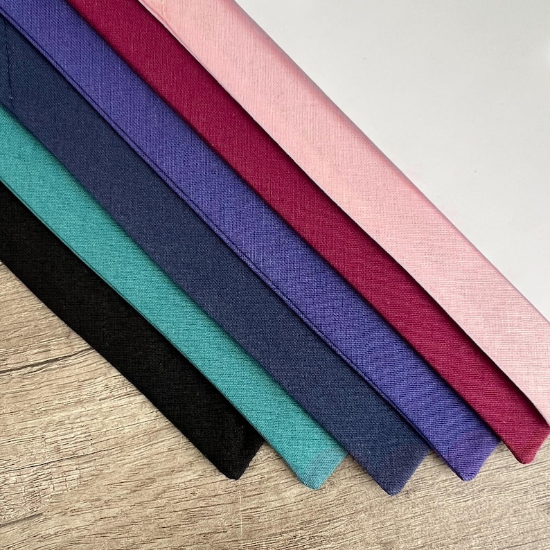 K&ouml;nnte beinhalten: Eine Sammlung von sechs rechteckigen Stoffmustern, die in einem diagonalen, &uuml;berlappenden Muster angeordnet sind. Die Farben umfassen Schwarz, T&uuml;rkis, Marineblau, Lila, Magenta und Hellrosa, alle mit einer sichtbaren Webstruktur.