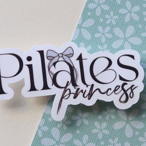 May include: White sticker with black text that reads "Pilates Princess" with a light blue bow on top.