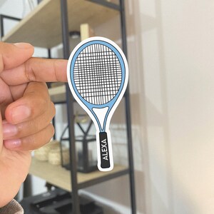 以下が含まれることがあります： ハンドルに「ALEXA」と印刷された青と白のテニスラケットのステッカーです。
