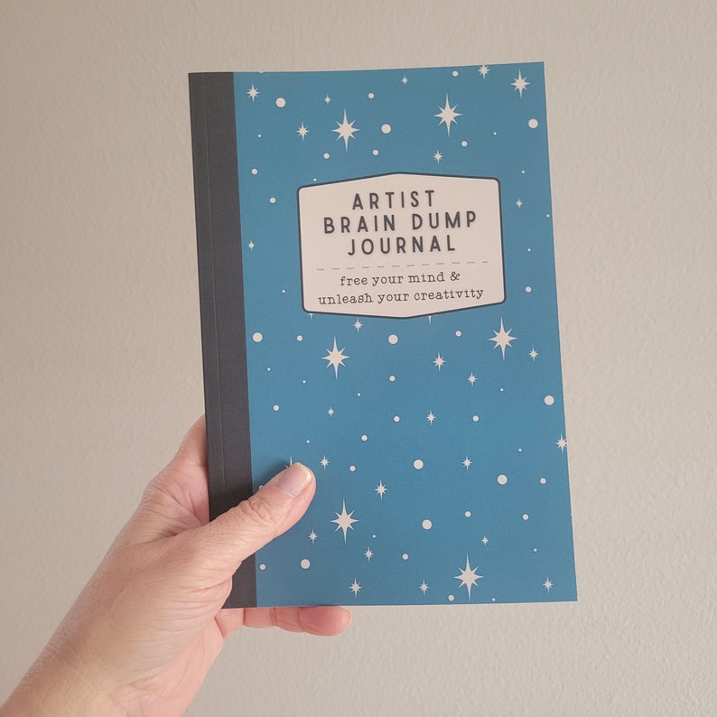 May include: A blue journal with white stars and the text "ARTIST BRAIN DUMP JOURNAL" and "free your mind & unleash your creativity" on the cover.